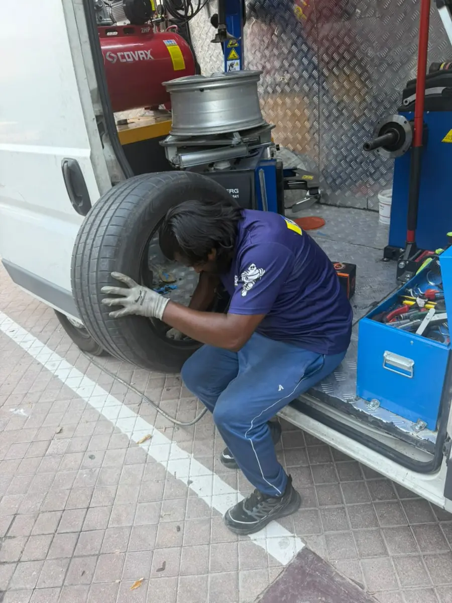 Mobile tyre technician fitting a replacement tyre beside the service van in Dubai